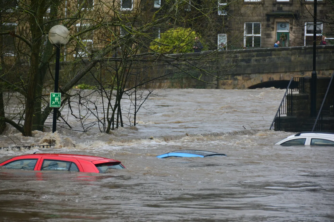 Tres vagones parcialmente sumergidos en un río inundado cerca de un puente de piedra