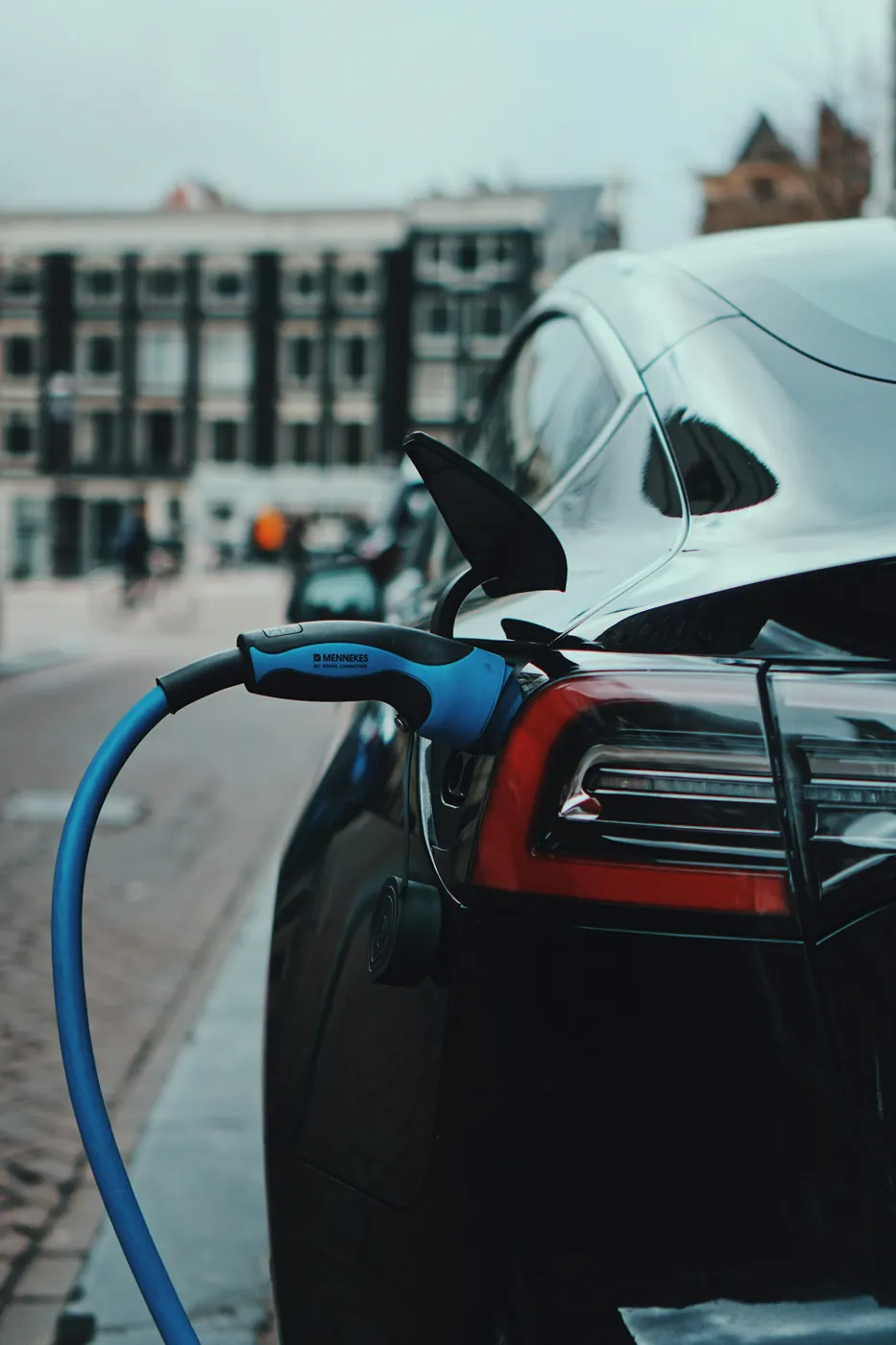 Un coche eléctrico negro cargando en una calle de la ciudad con un cable azul